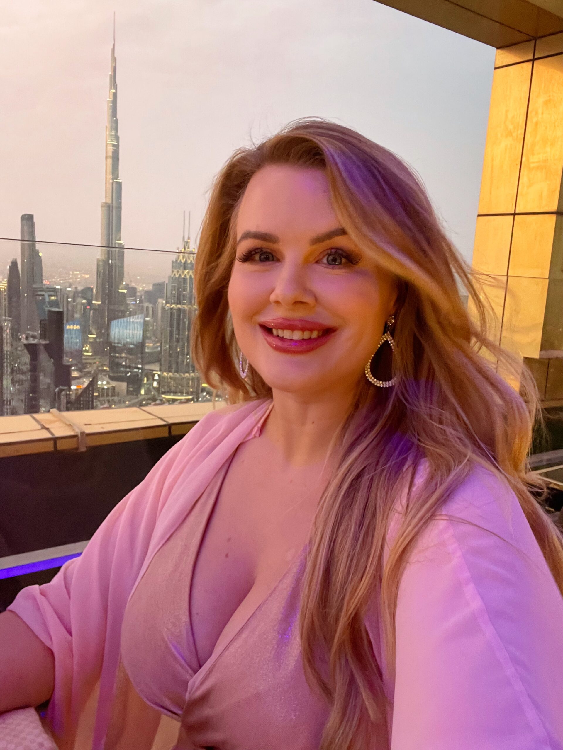 Travel creator Lilli Luxe smiling on a rooftop in Dubai with the city skyline in the background.