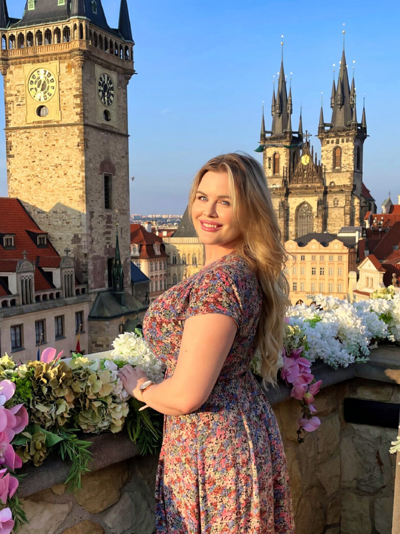 Lilli Luxe posing on a rooftop terrace overlooking Prague's historic Old Town and church spires.
